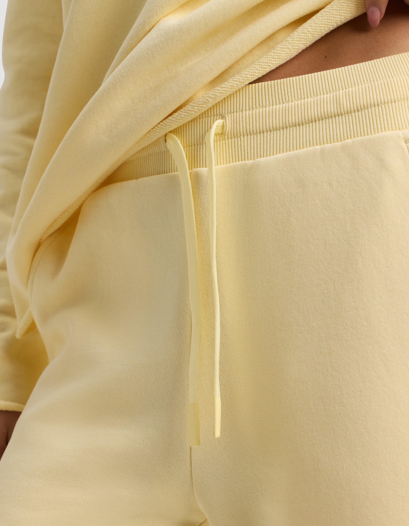 Close-up of a person wearing the Women's Chelsea Cropped Pant by Cozy Earth in light yellow, featuring a matching drawstring and paired with a yellow sweatshirt slightly lifted to reveal the waistband.