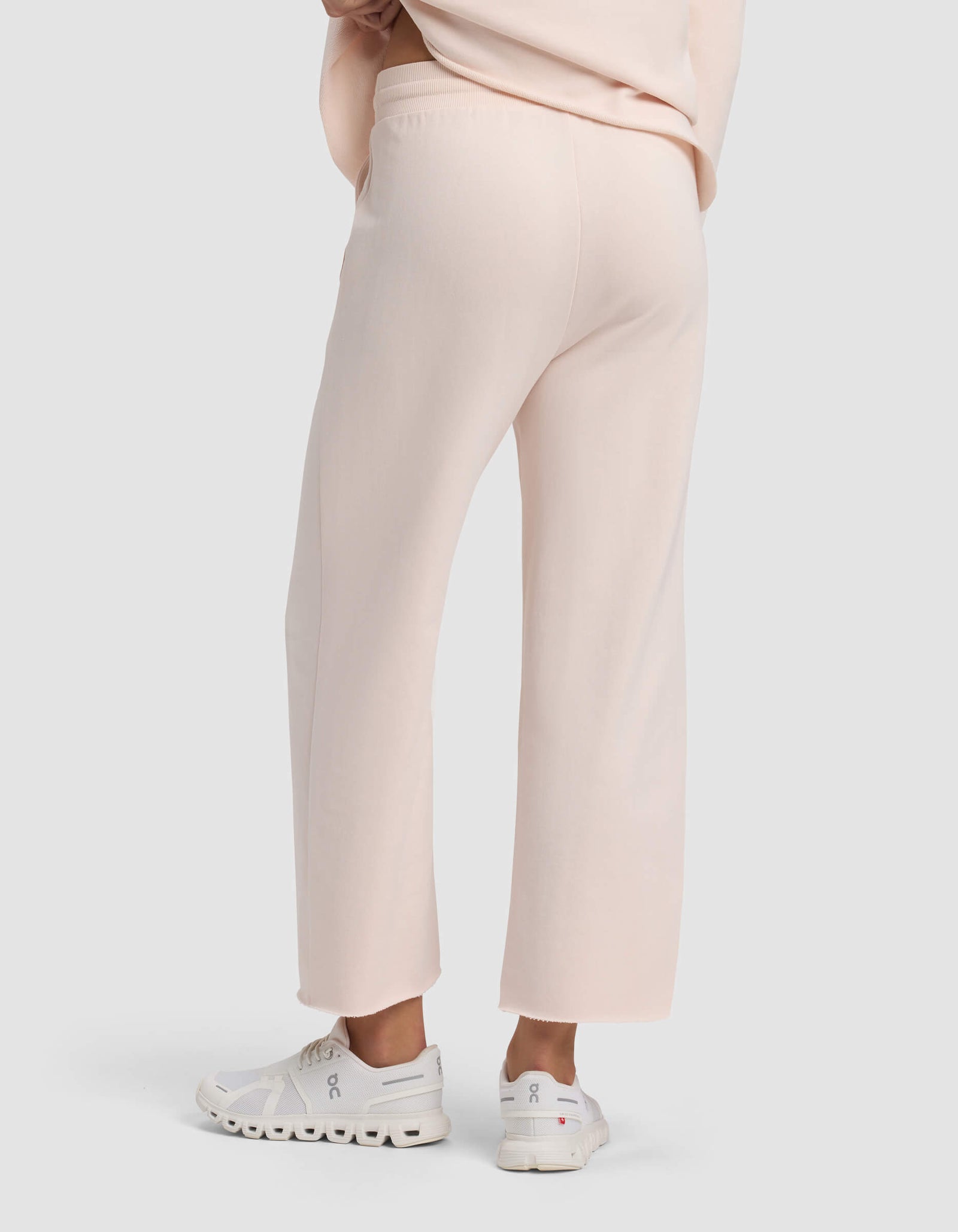 A person is shown from the waist down, facing away, wearing Cozy Earth Women's Chelsea Cropped Pant in light pink and white athletic shoes against a plain light background.