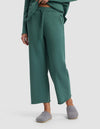A person wears the Cozy Earth Women's Chelsea Cropped Pant in green with a drawstring, a matching top partly visible, and gray slippers, standing against a plain light gray background.|Color:Sea Green