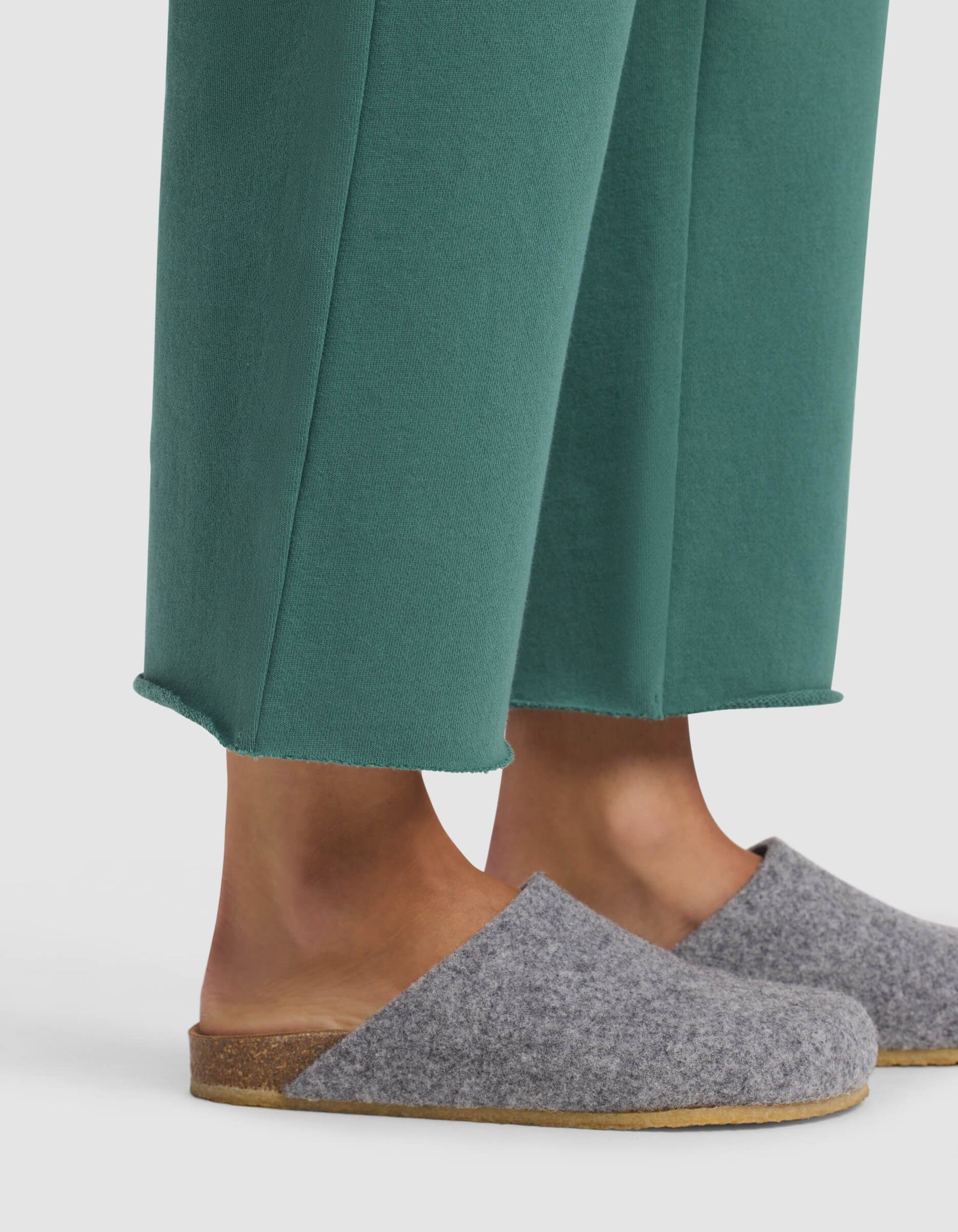 A person wearing Cozy Earth's Women's Chelsea Cropped Pant in green and gray wool slip-on slippers with cork soles, standing against a white background.