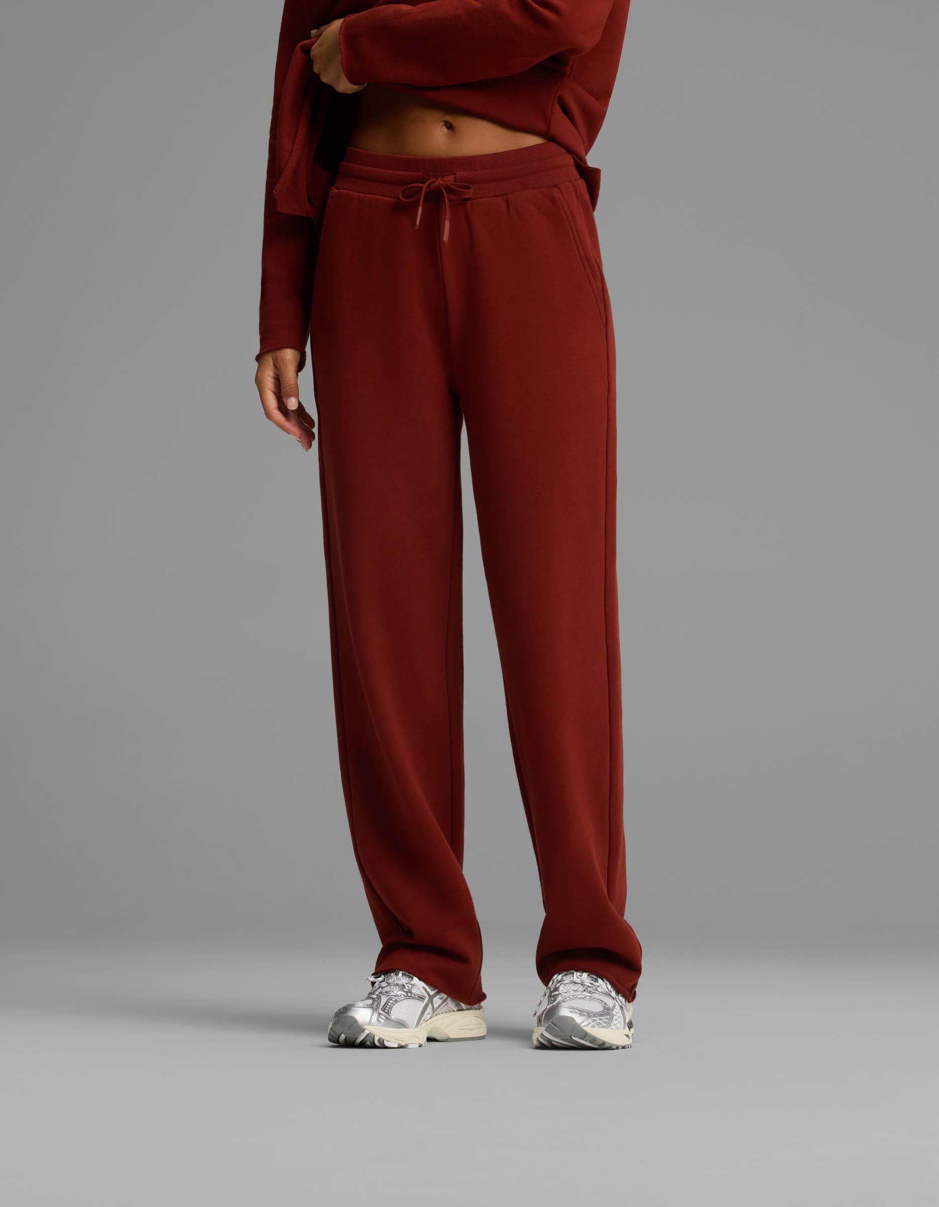 A person wearing the Women's Chelsea Set by Cozy Earth in maroon, paired with silver sneakers, stands against a plain gray background. The person's face is not visible.|Color:Currant