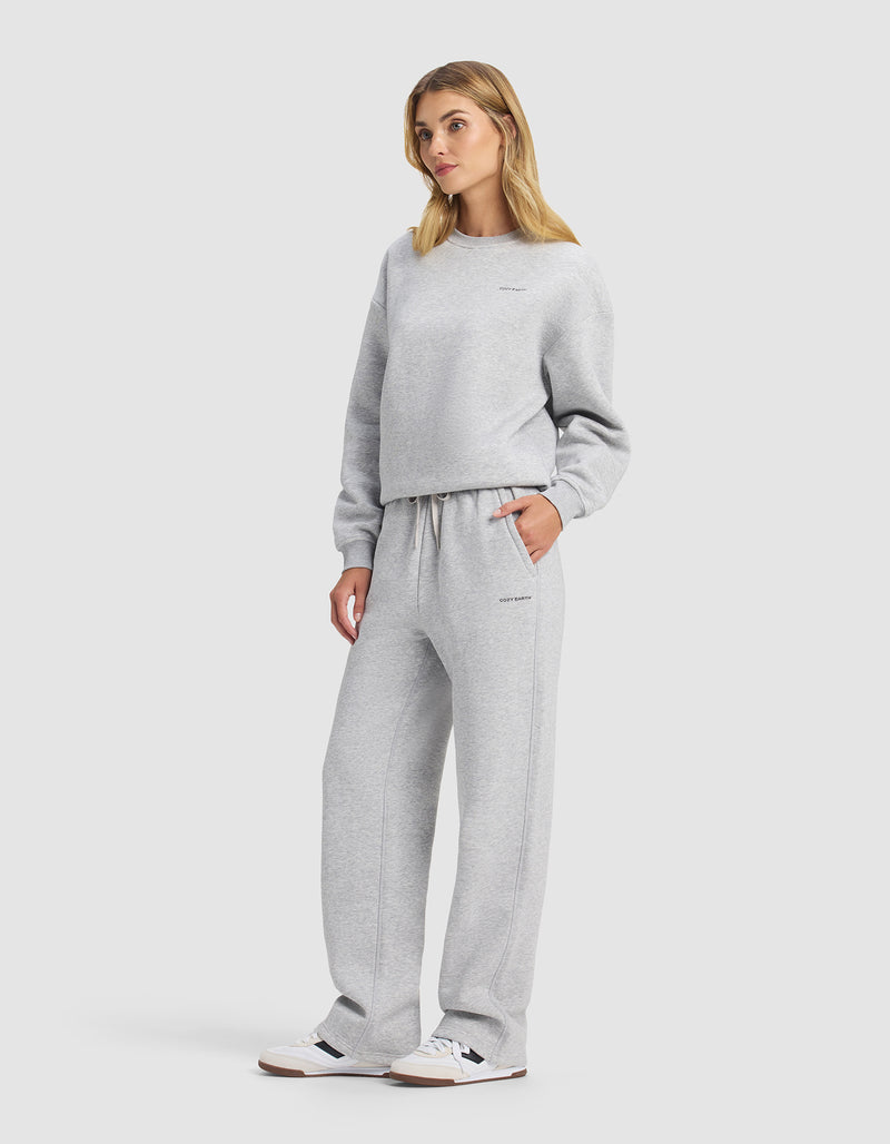 A woman wears the Cozy Earth Women's Cityscape 2.0 Crewneck & Wide Leg Pant Set in light gray with white sneakers, hands in pockets, blonde hair, standing against a plain white background.