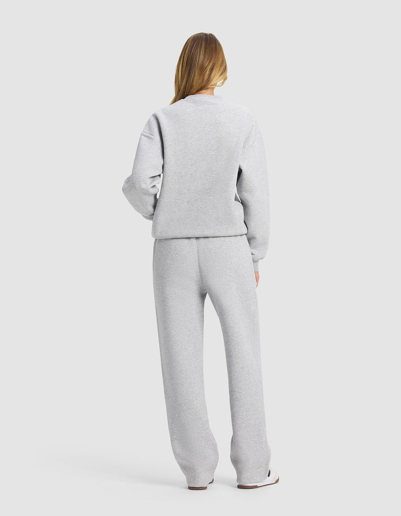 A woman with long hair, seen from behind, wears the Cozy Earth Women's Cityscape 2.0 Crewneck & Wide Leg Pant Set in light gray, standing against a plain matching background.