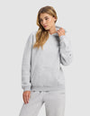 A woman wears the Cozy Earth Women's Cityscape 2.0 Hoodie in light gray, standing against a plain background and looking to the side as she adjusts her collar.|Color:Heather Grey