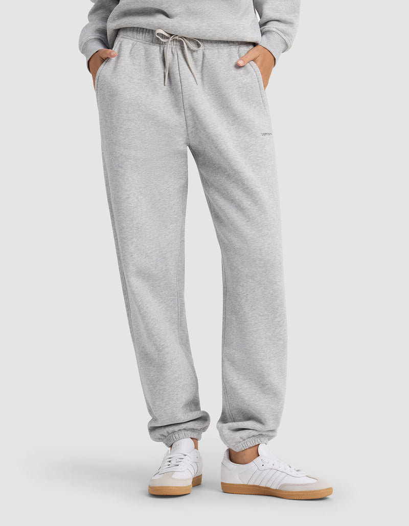 A person wears Cozy Earth's Women's Cityscape 2.0 Sweatpant in light gray with an elastic waistband and drawstring, paired with white sneakers and a matching sweatshirt, hands in pockets.