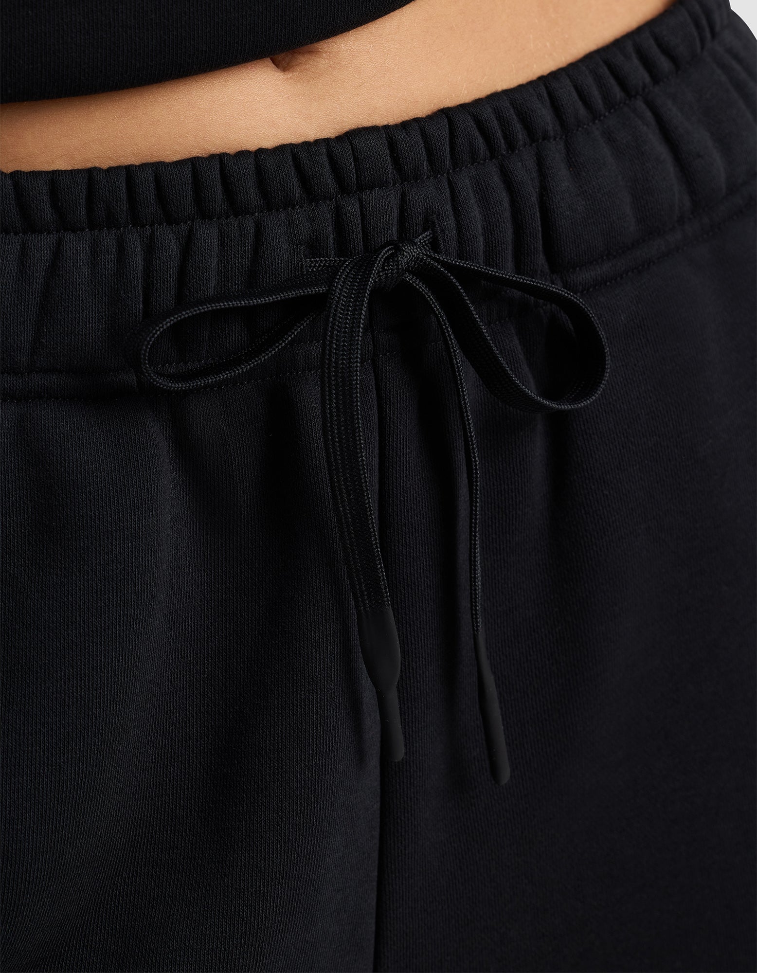 Close-up of a person wearing Cozy Earth's Women's Cityscape 2.0 Sweatpant, featuring an elastic waistband with a tied drawstring, paired with a black top and showing part of their midriff.
