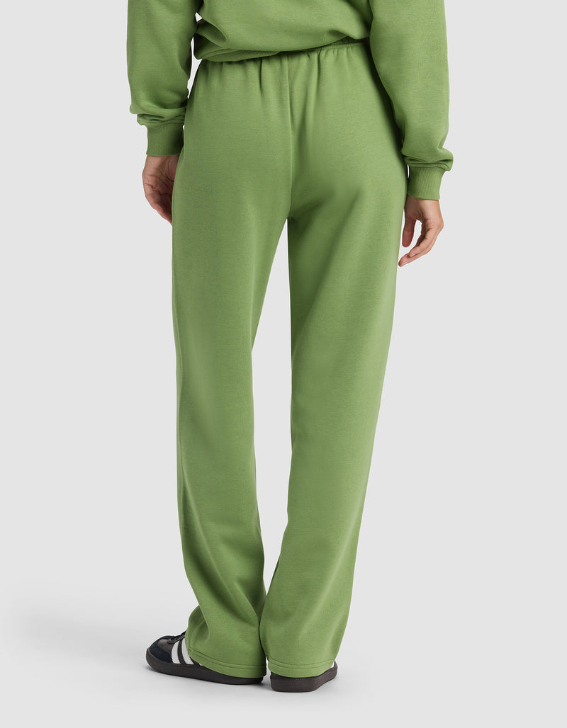 A person is seen from the back wearing the Cozy Earth Women's Cityscape 2.0 Wide Leg Pant in light green with a matching sweatshirt and black sandals with white stripes, set against a plain, light-colored background.