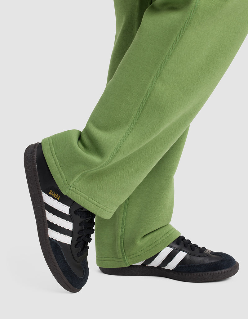 A person wearing Cozy Earth Women's Cityscape 2.0 Wide Leg Pants and black Adidas Samba sneakers with white stripes stands with one foot crossed over the other on a light grey background.