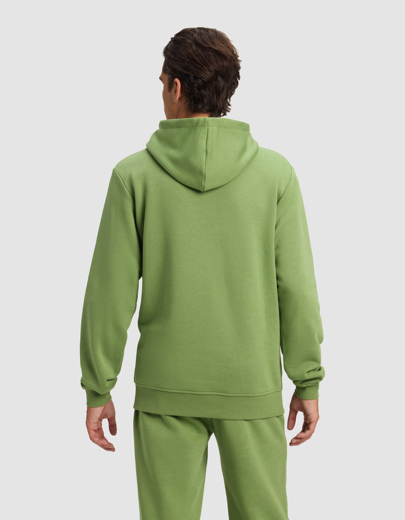 A man with short brown hair is seen from behind wearing the Cozy Earth Men's Cityscape 2.0 Hoodie in light green, paired with matching sweatpants, standing against a plain light gray background.