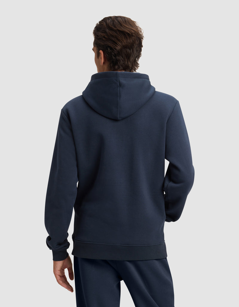 A man with short brown hair is seen from behind wearing Cozy Earth's Men's Cityscape 2.0 Hoodie in dark blue, paired with matching pants, set against a plain light gray background.
