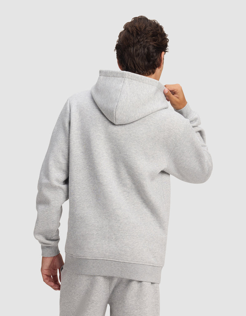 A person is seen from behind wearing the Cozy Earth Men's Cityscape 2.0 Hoodie in light gray, holding the hood against a plain, light background.