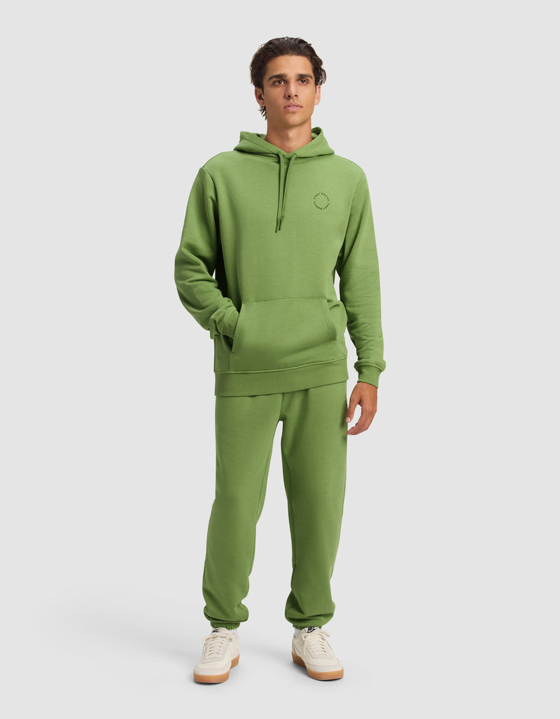 A young man wears the Cozy Earth Men's Cityscape 2.0 Hoodie & Sweatpant Set with white sneakers, standing against a plain background with his hands in the hoodie pocket and a neutral expression.