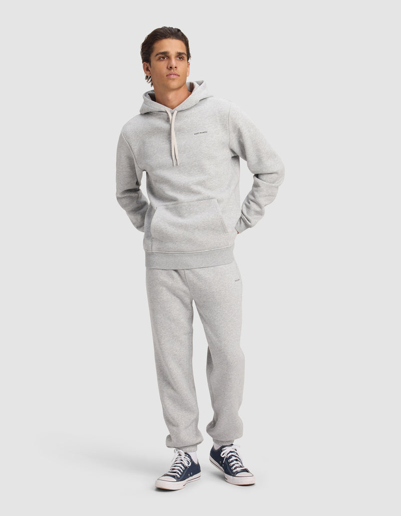 A young man models the Cozy Earth Men's Cityscape 2.0 Hoodie & Sweatpant Set in light gray, standing against a plain background with his hands in his pockets and navy blue sneakers, looking slightly to the side.