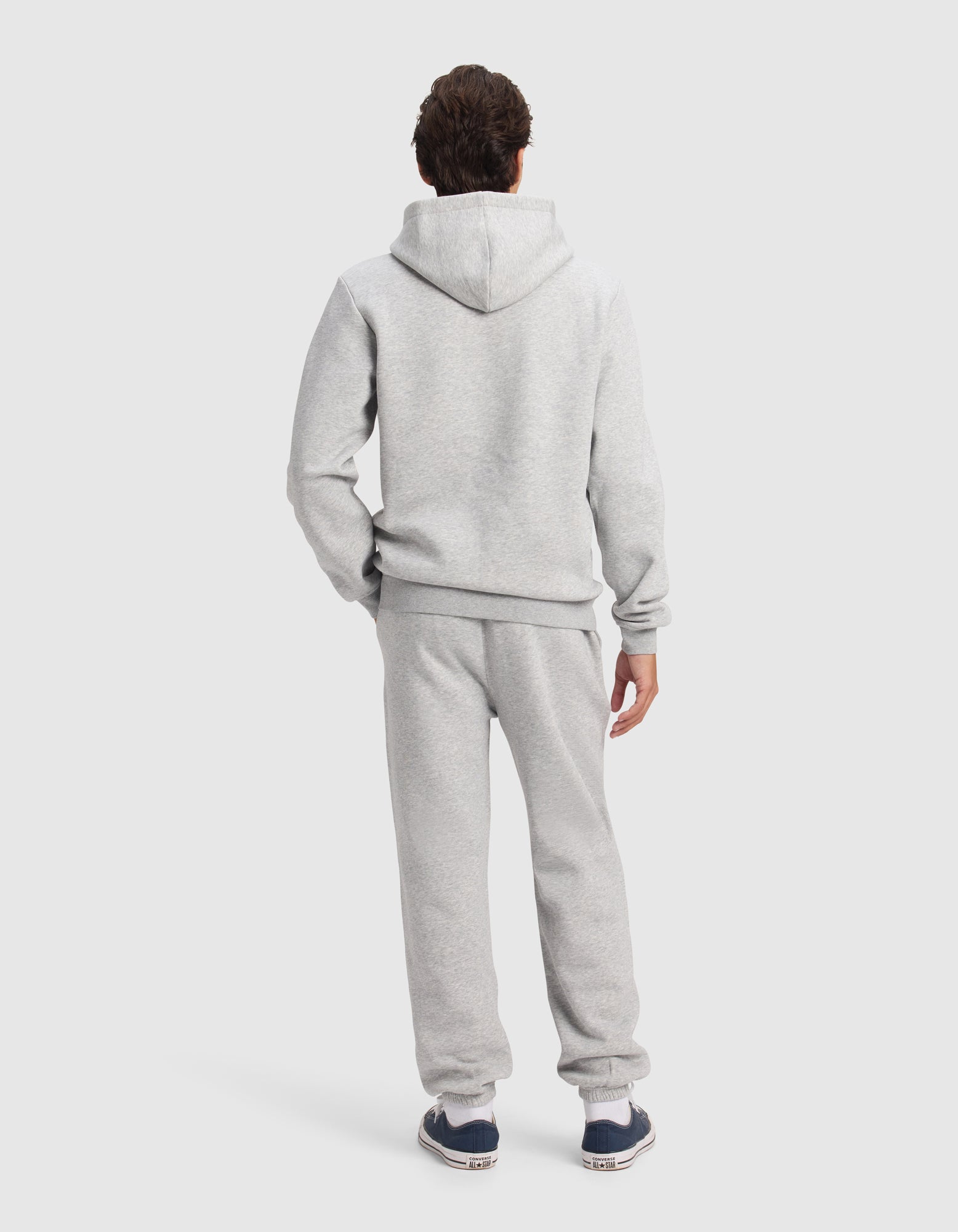 A person faces away from the camera in Cozy Earth's Men's Cityscape 2.0 Hoodie & Sweatpant Set, paired with dark sneakers, shown against a plain light background.