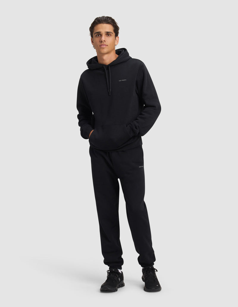 A young man faces forward in the Cozy Earth Men's Cityscape 2.0 Hoodie & Sweatpant Set, paired with black sneakers. His hands are in the hoodie pocket as he stands against a plain light gray background.