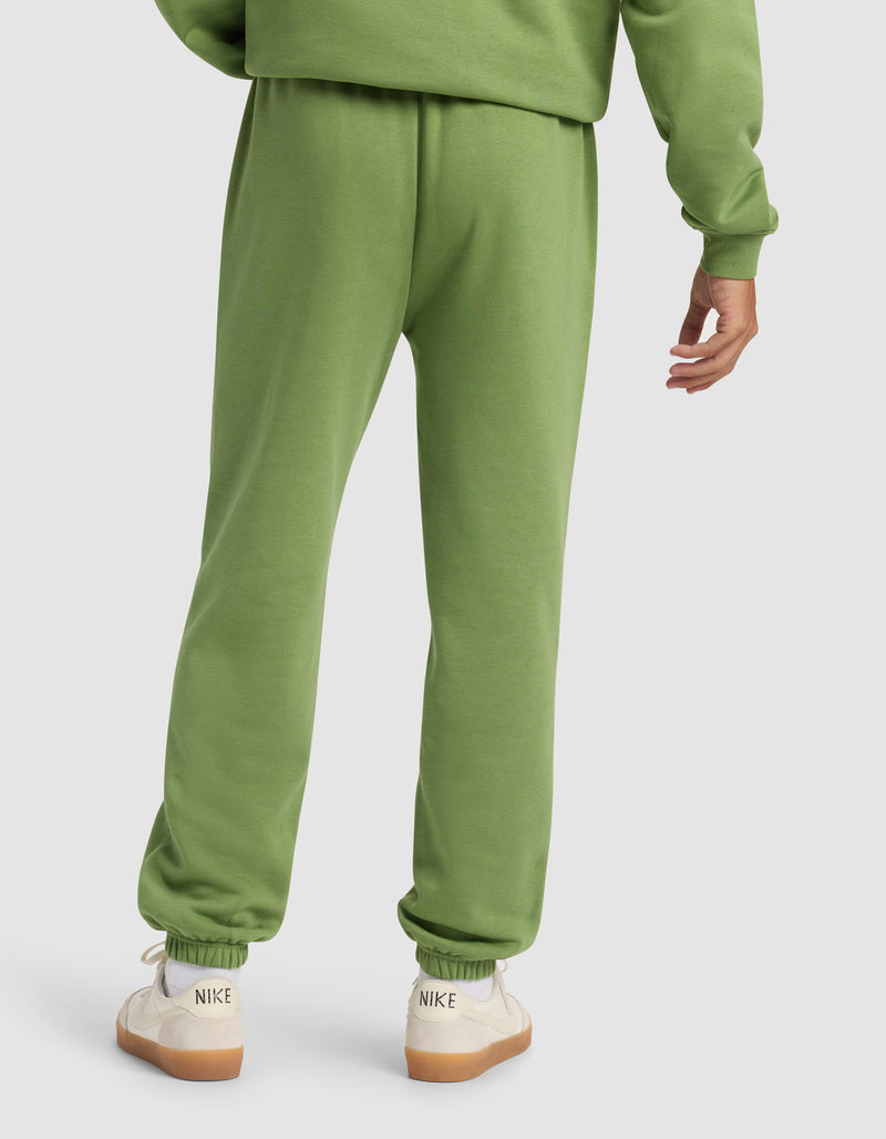 A person is shown from the back wearing Cozy Earth Men's Cityscape 2.0 Sweatpant and a matching green sweatshirt, paired with white Nike sneakers with beige soles against a plain, light-colored background.