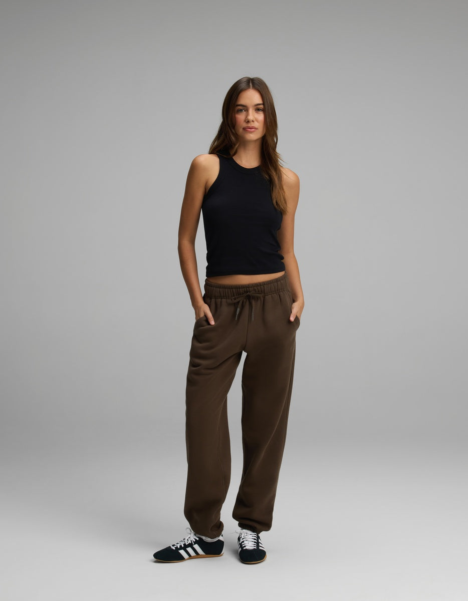 A woman wearing a black tank top and brown Women’s CityScape Sweatpant with a drawstring waist, paired with black and white sneakers.