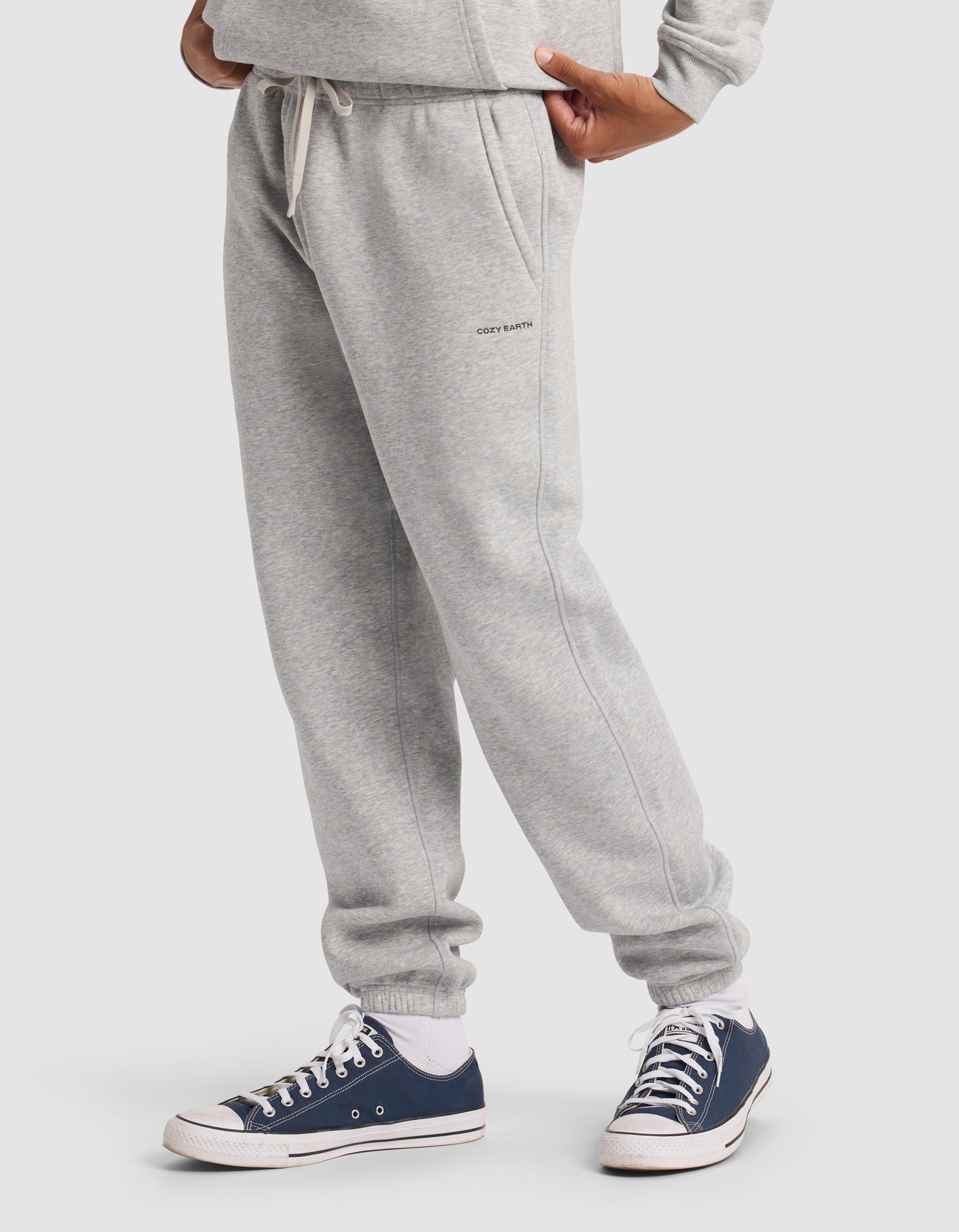 A person wearing Cozy Earth Men's Cityscape 2.0 Sweatpant in light gray with a matching sweatshirt and navy blue and white sneakers, standing against a plain white background; only the lower body is visible.