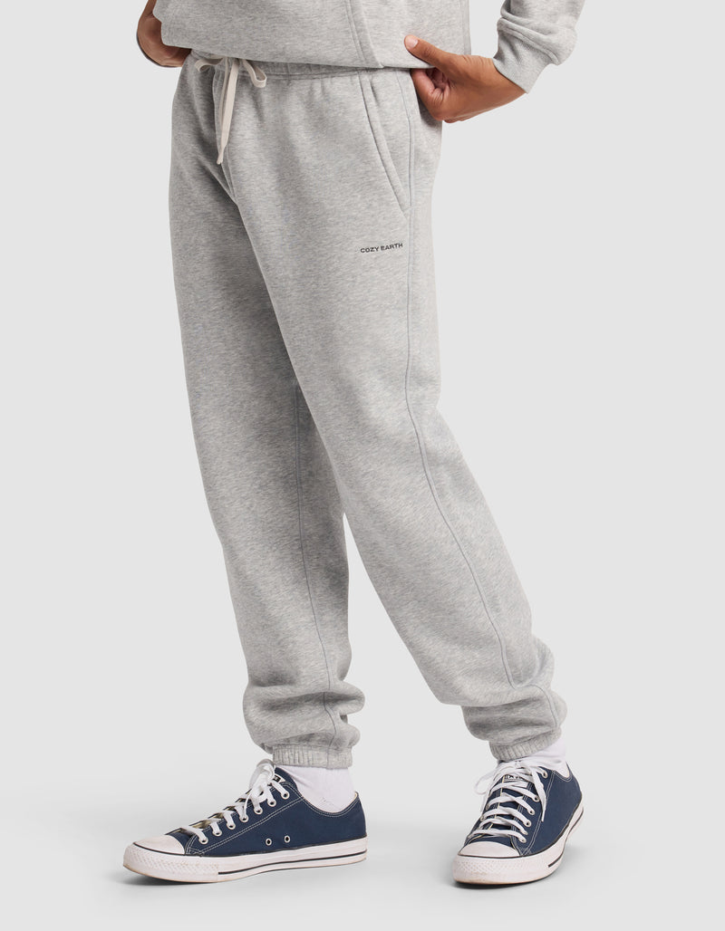 A person wearing Cozy Earth Men's Cityscape 2.0 Sweatpant in light gray with a matching sweatshirt and navy blue and white sneakers, standing against a plain white background; only the lower body is visible.