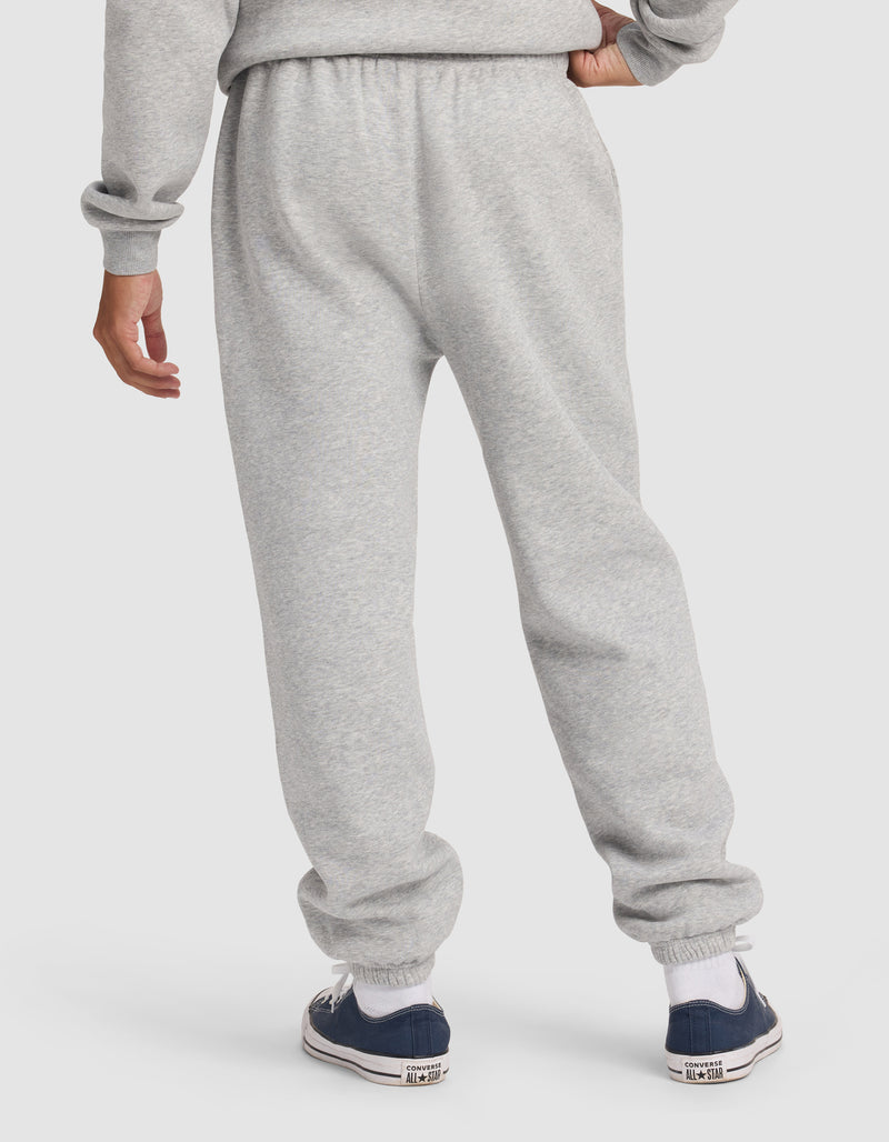 A person is seen from behind wearing Cozy Earth's Men's Cityscape 2.0 Sweatpant in light gray, paired with a matching sweatshirt, white socks, and navy blue sneakers against a plain backdrop.