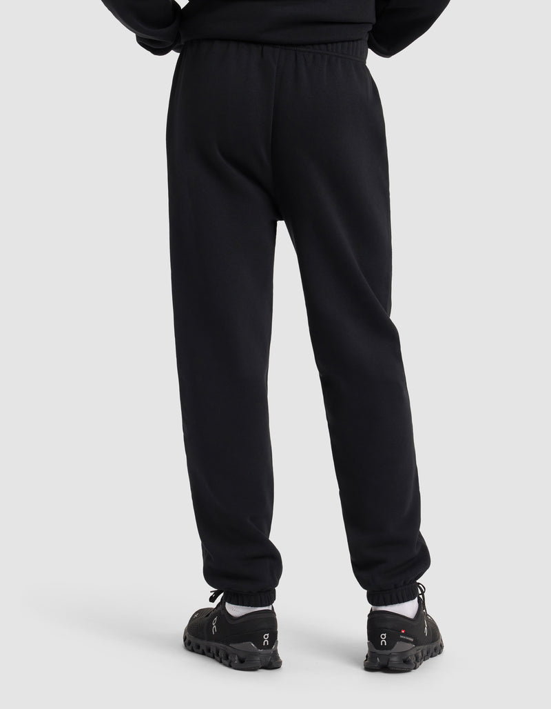 A person wearing Cozy Earth Men's Cityscape 2.0 Sweatpant in black and black athletic shoes is shown from the back, standing against a plain light grey background.