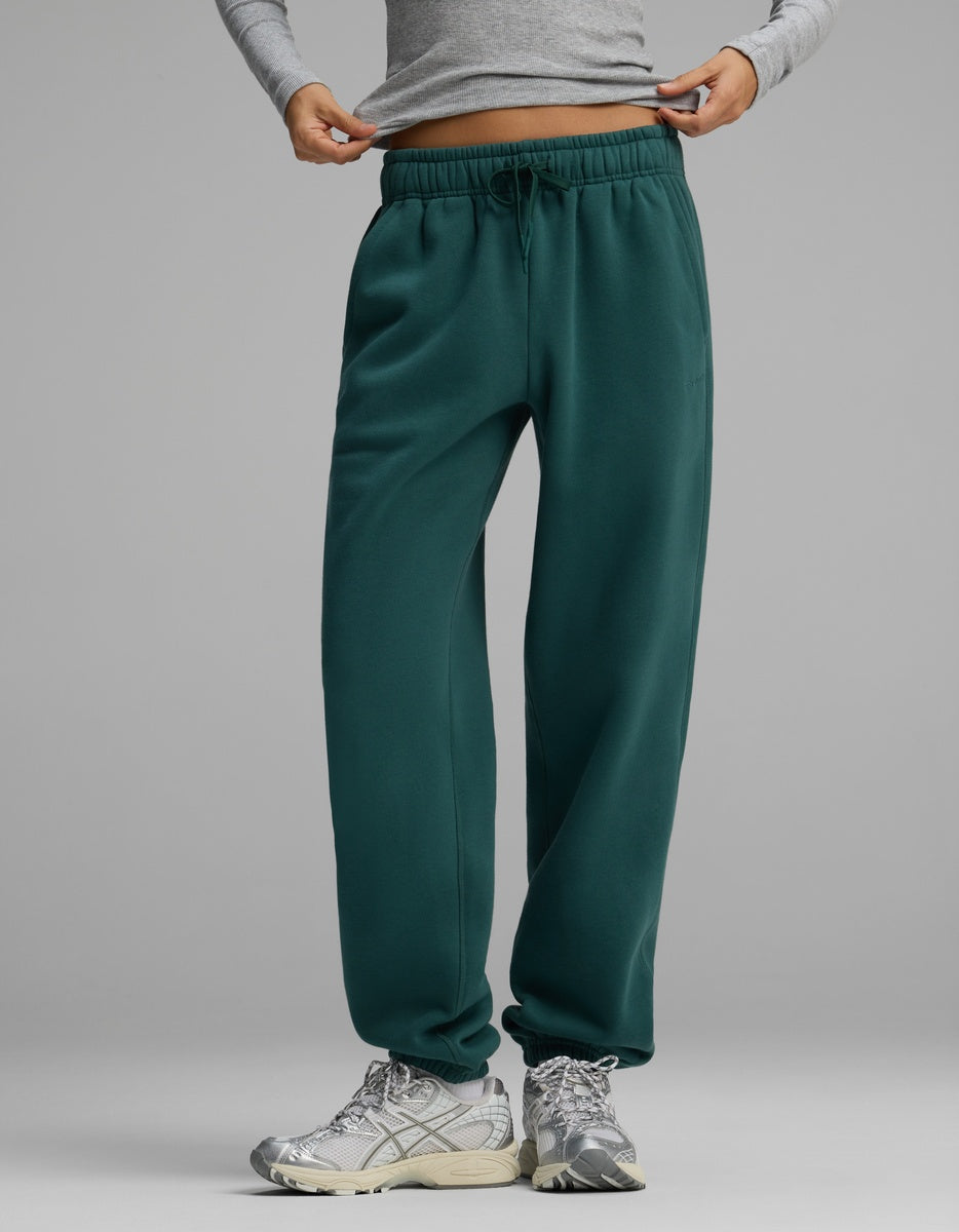 Cozy Earth Women’s CityScape Sweatpant in dark green with an elastic waistband and drawstring, paired with silver athletic sneakers.