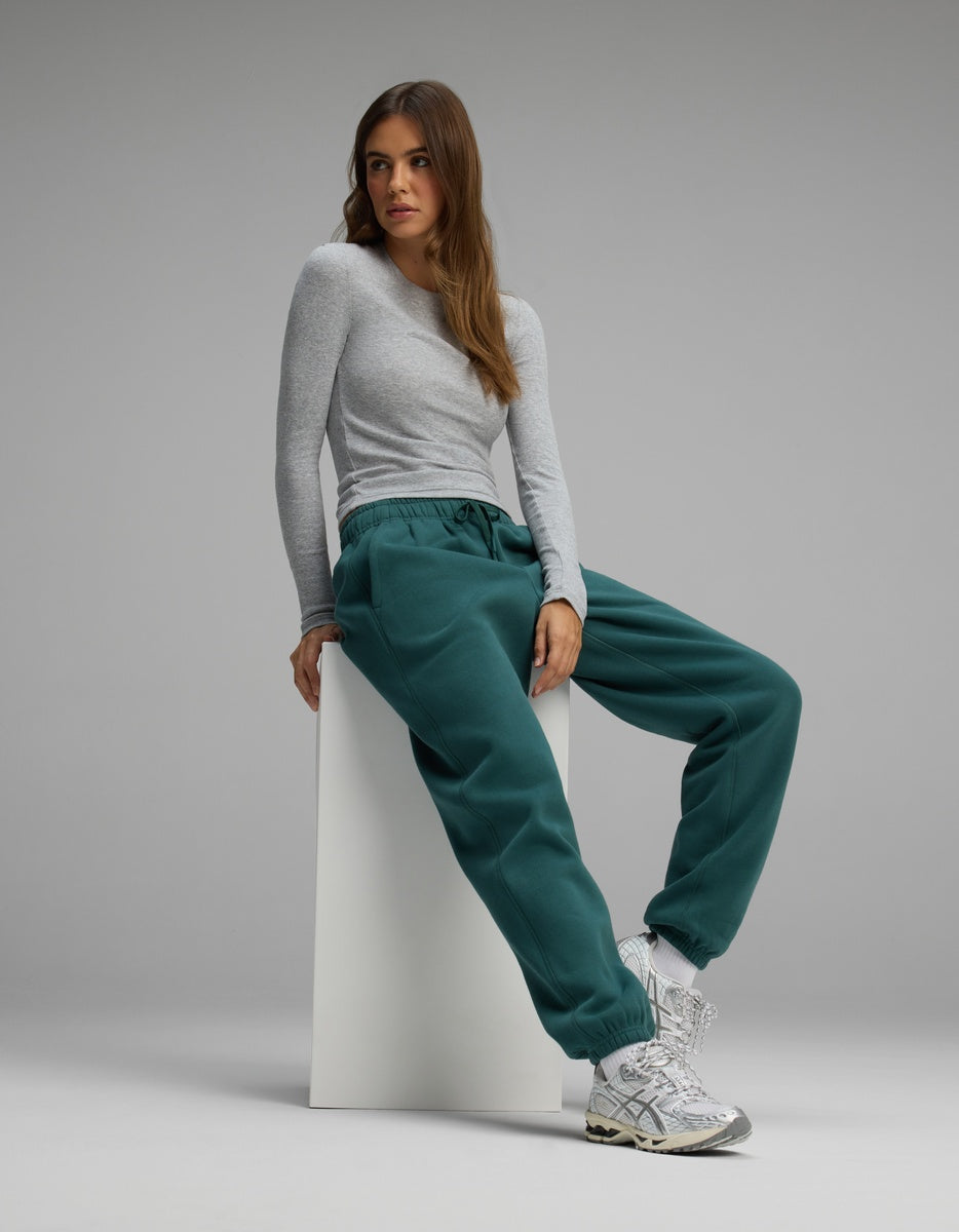A woman wearing a gray long-sleeved shirt and dark teal Women’s CityScape Sweatpant sits on a white block.