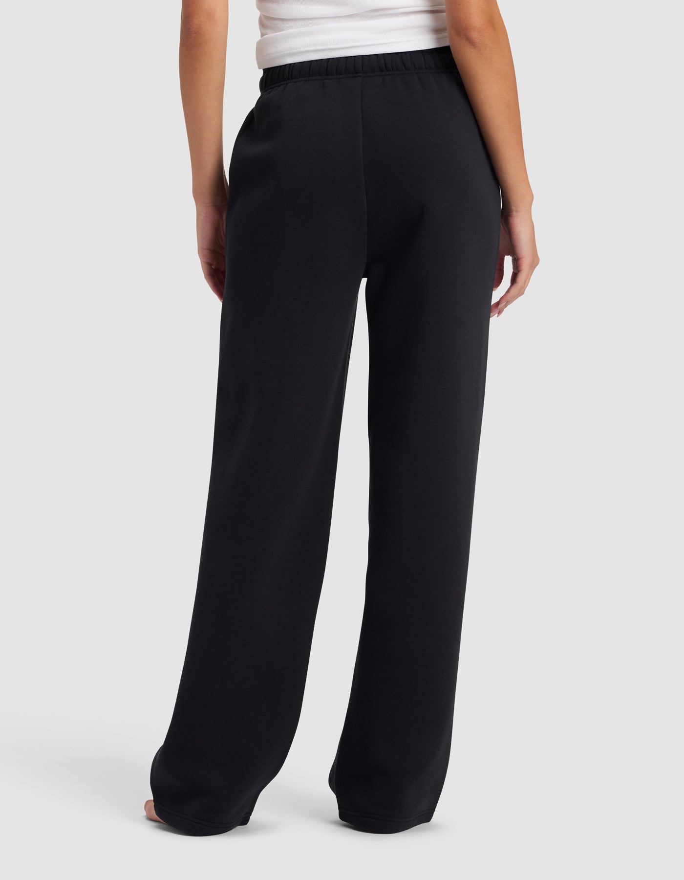 A person stands barefoot, facing away from the camera against a light gray background, wearing a white top and Cozy Earth's Women's Cityscape 2.0 Wide Leg Pant in black.