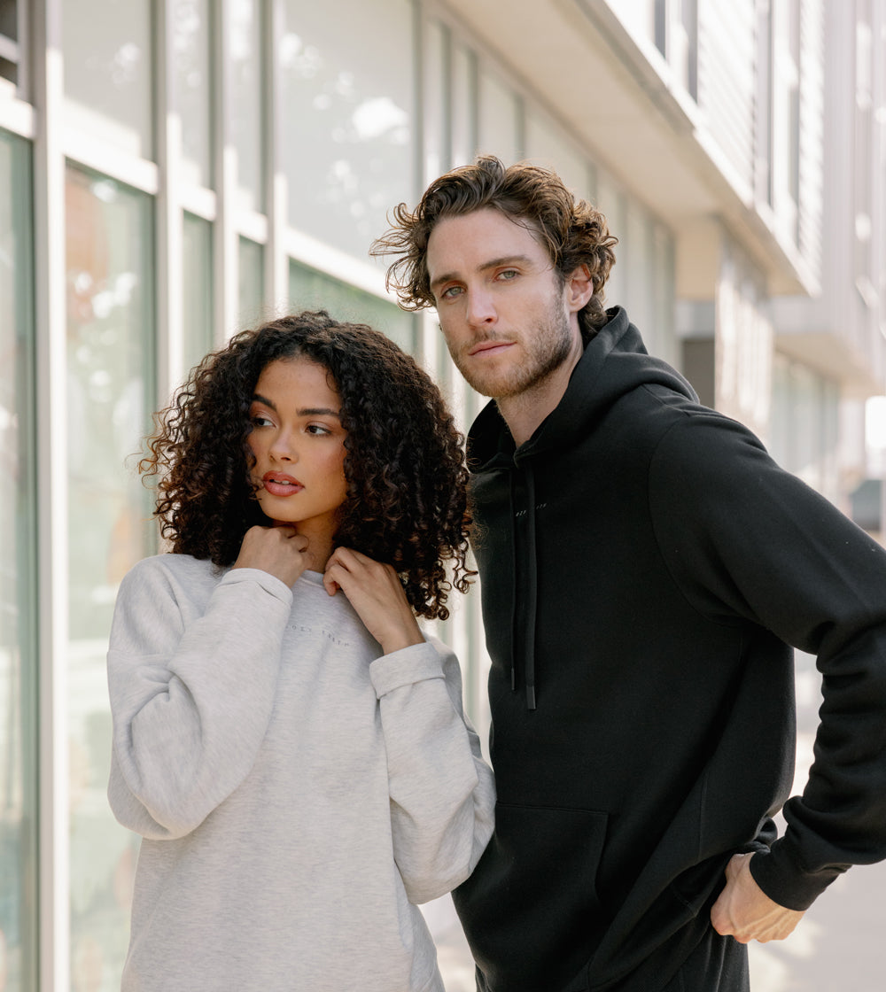 A man and woman standing close to each other outdoors with a modern building in the background. They wear Cozy Earth Cityscape Sweatpants and hoodies.