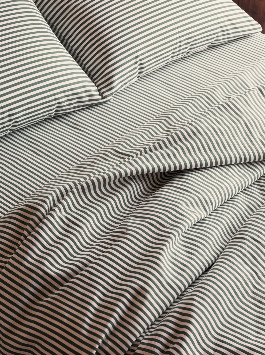 Close-up of striped bedding with matching pillows, showing a duvet or comforter in a dark green and off-white stripe pattern.