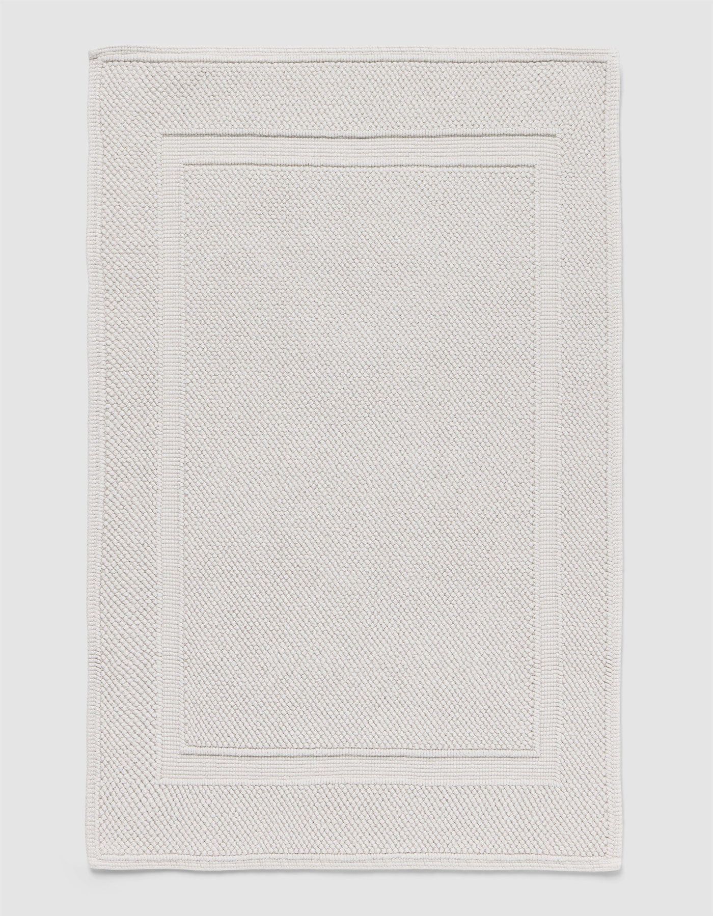 The Cozy Earth Classic Bath Mat features a rectangular shape, light color, subtle textured pattern, and elegant double border design on the edges.