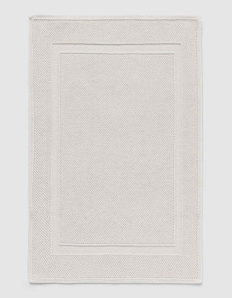The Cozy Earth Classic Bath Mat features a rectangular shape, light color, subtle textured pattern, and elegant double border design on the edges.