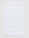 The Cozy Earth Classic Bath Mat in white features a textured surface with a subtle border pattern and is shown flat against a neutral background.|Color:White