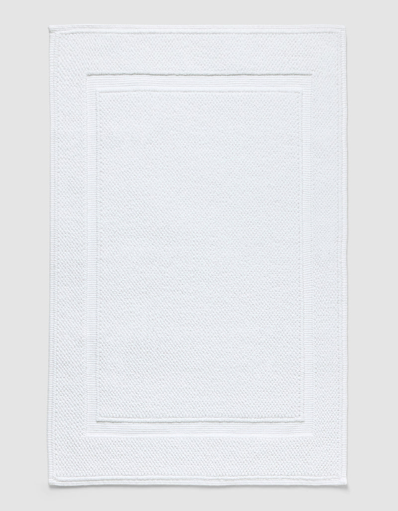 The Cozy Earth Classic Bath Mat in white features a textured surface with a subtle border pattern and is shown flat against a neutral background.