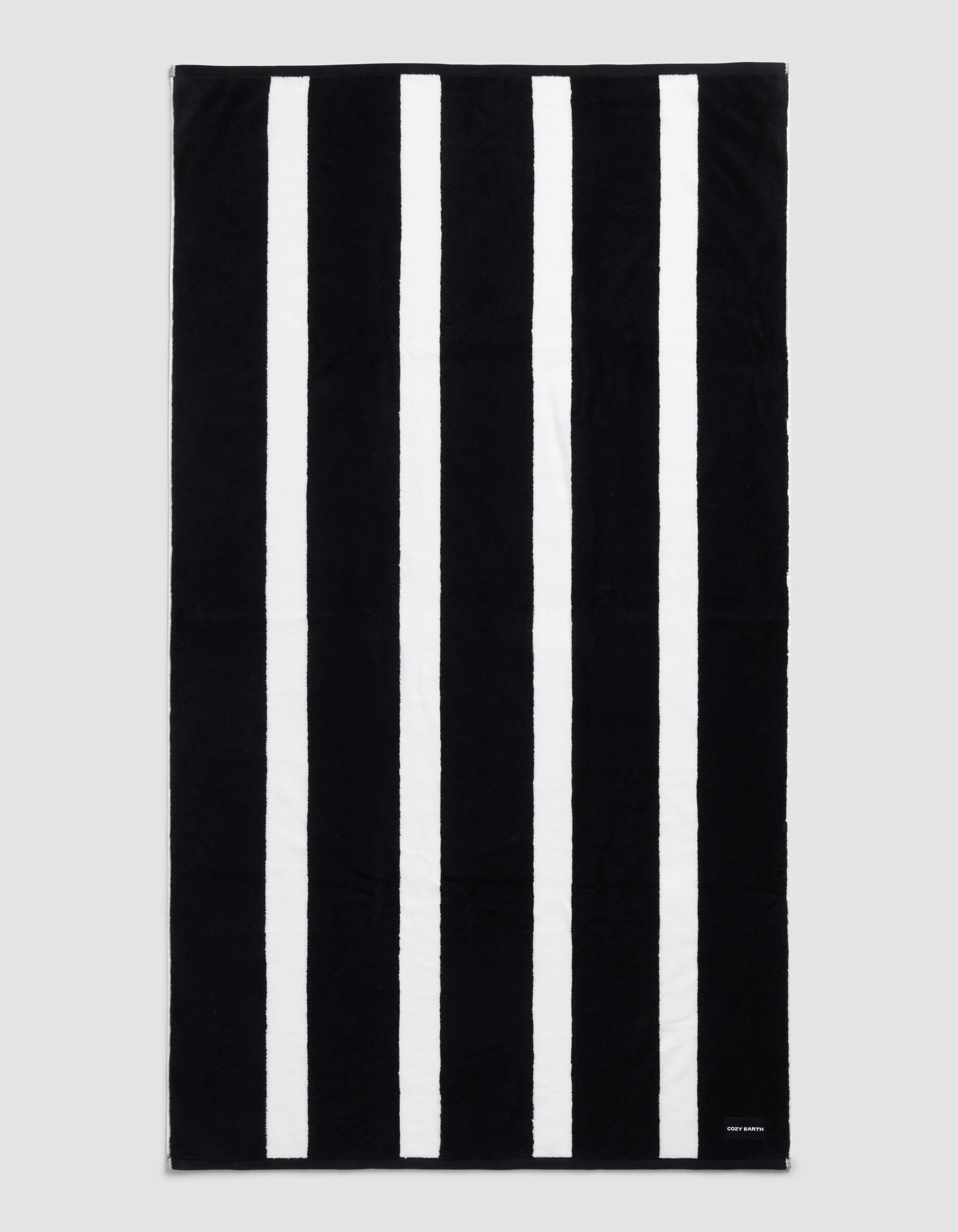 The Cozy Earth Classic Stripe Resort Towel in Jet Black is rectangular with five evenly spaced white stripes and a small white tag with text in the bottom right corner.