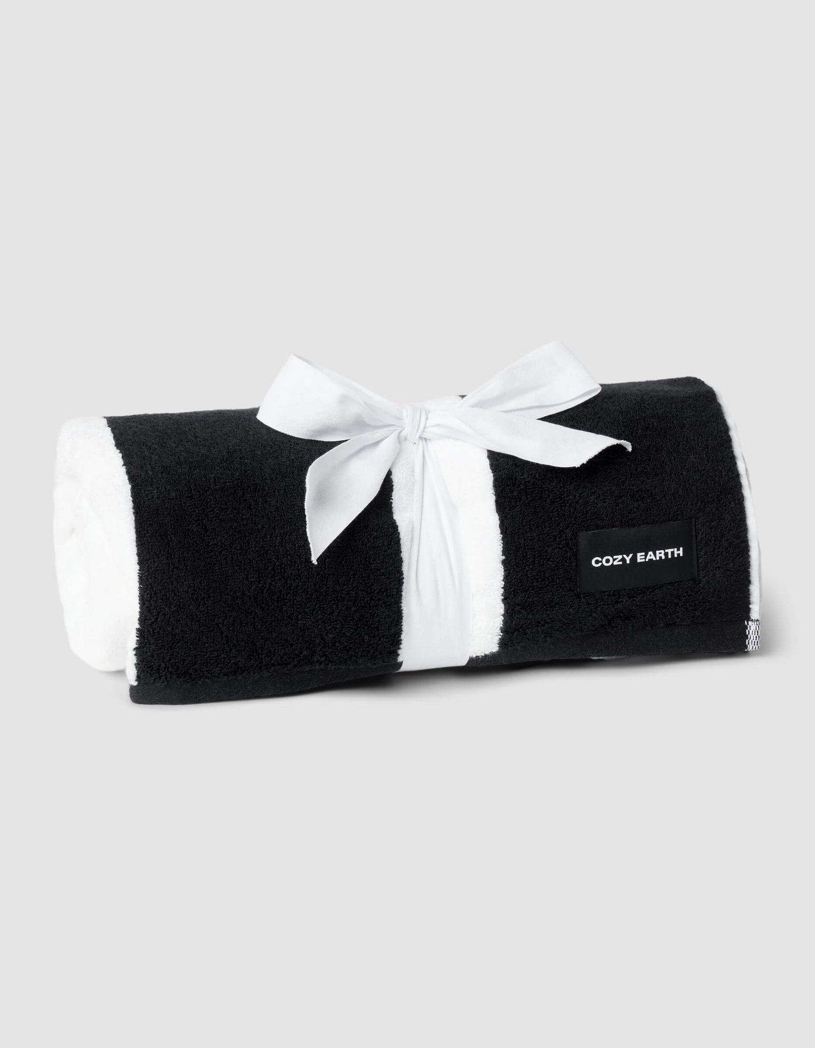 A rolled Classic Stripe Resort Towel by Cozy Earth, tied with a white ribbon and labeled on the edge, is displayed against a plain light gray background.