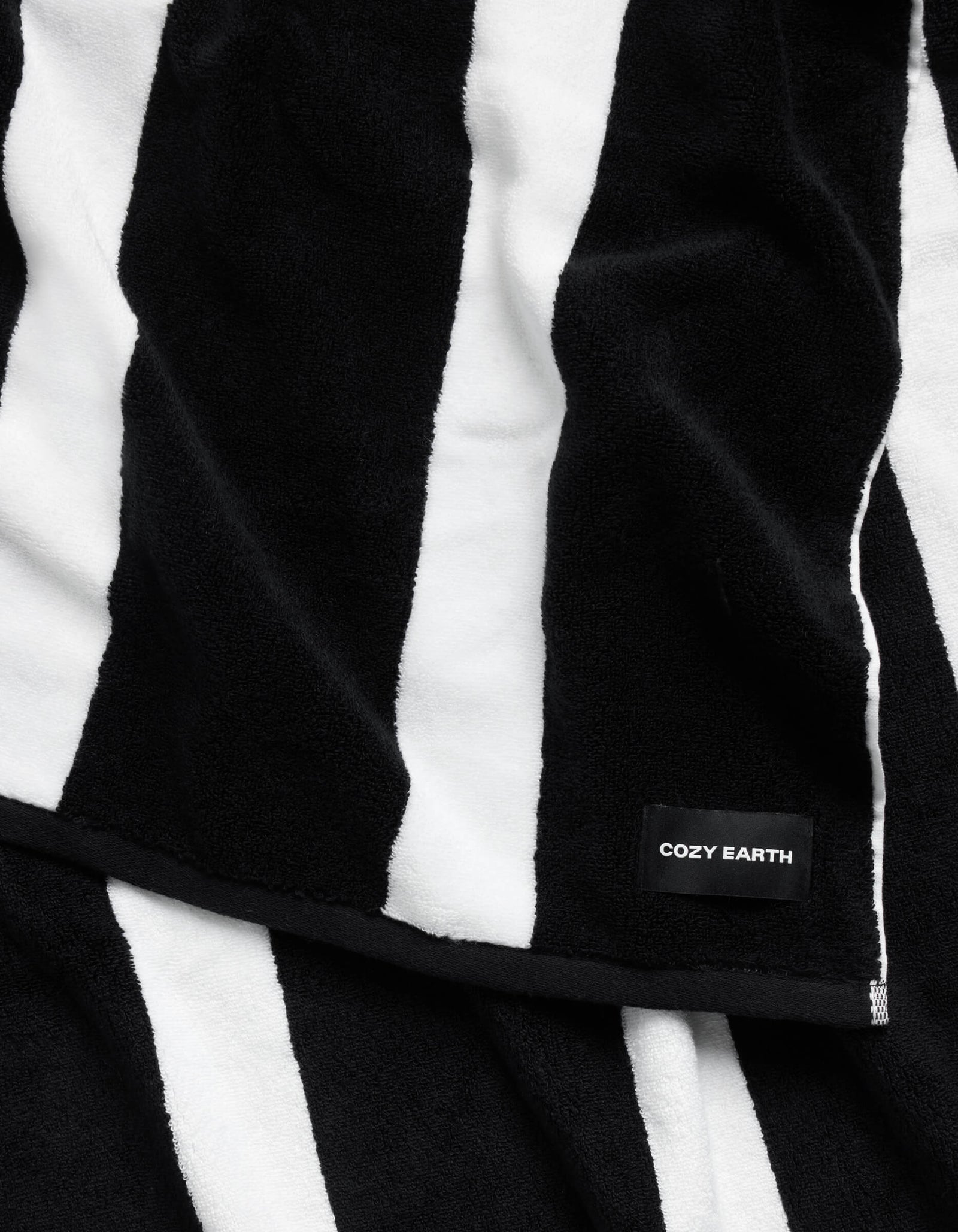 A plush Classic Stripe Resort Towel by Cozy Earth, featuring bold black and white stripes and a small black label in one corner with "COZY EARTH" in white text.