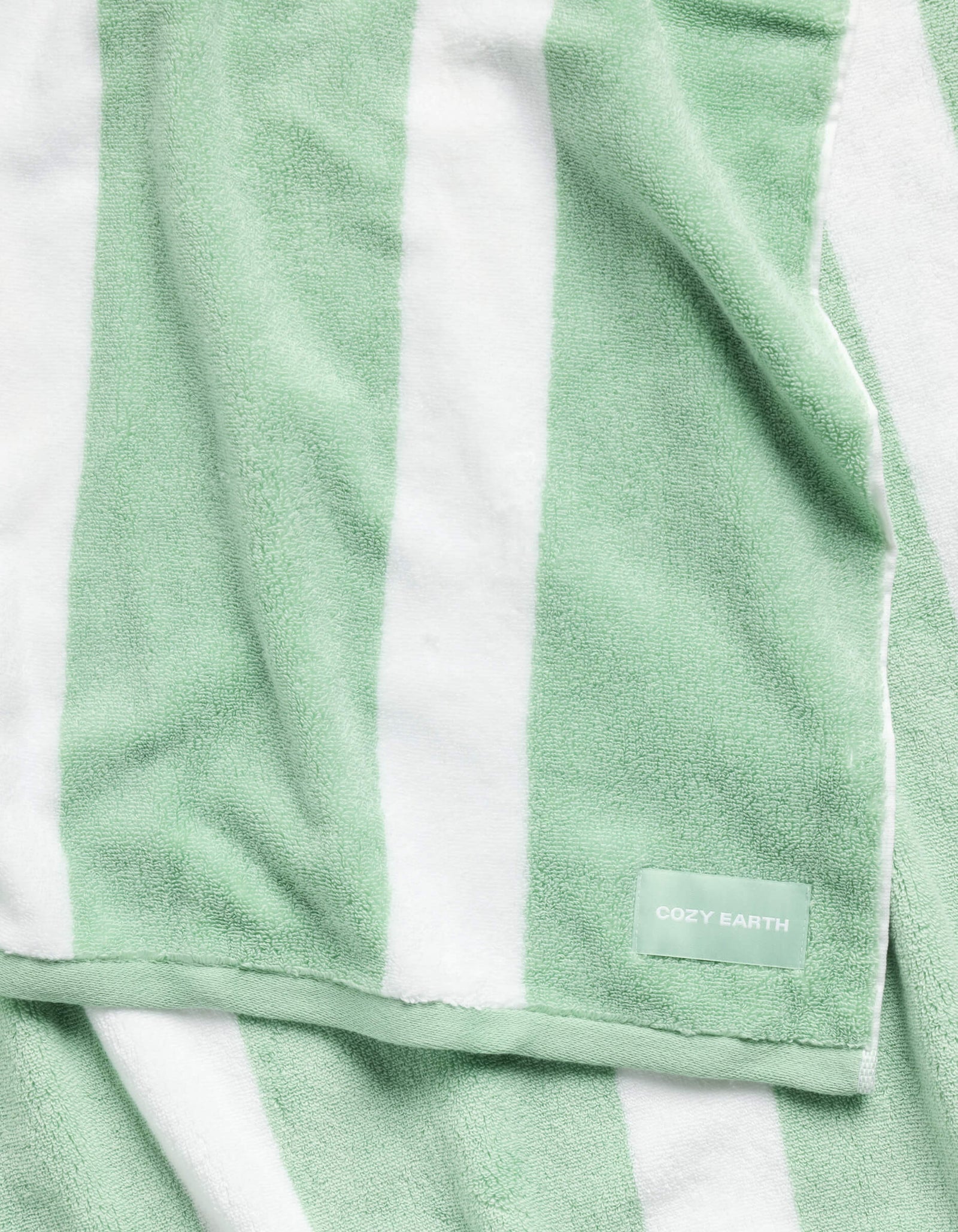 The Classic Stripe Resort Towel by Cozy Earth is a plush towel with wide green and white stripes and a small "Cozy Earth" label in one corner. It appears soft and partially folded.
