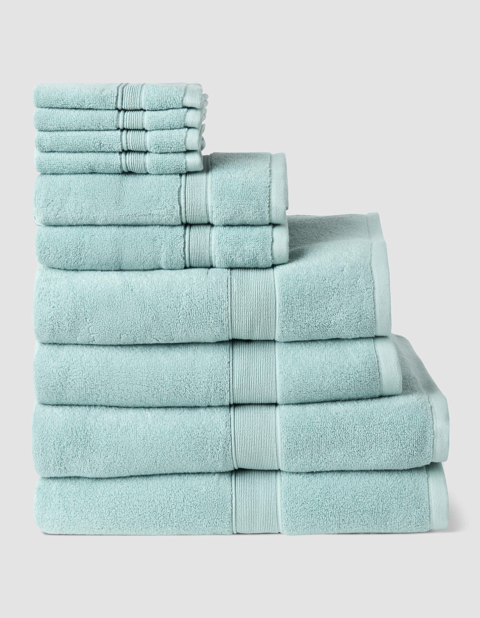 The Complete Luxe Bath Bundle by Cozy Earth features neatly stacked light blue towels in various sizes, arranged from largest to smallest against a plain light background.