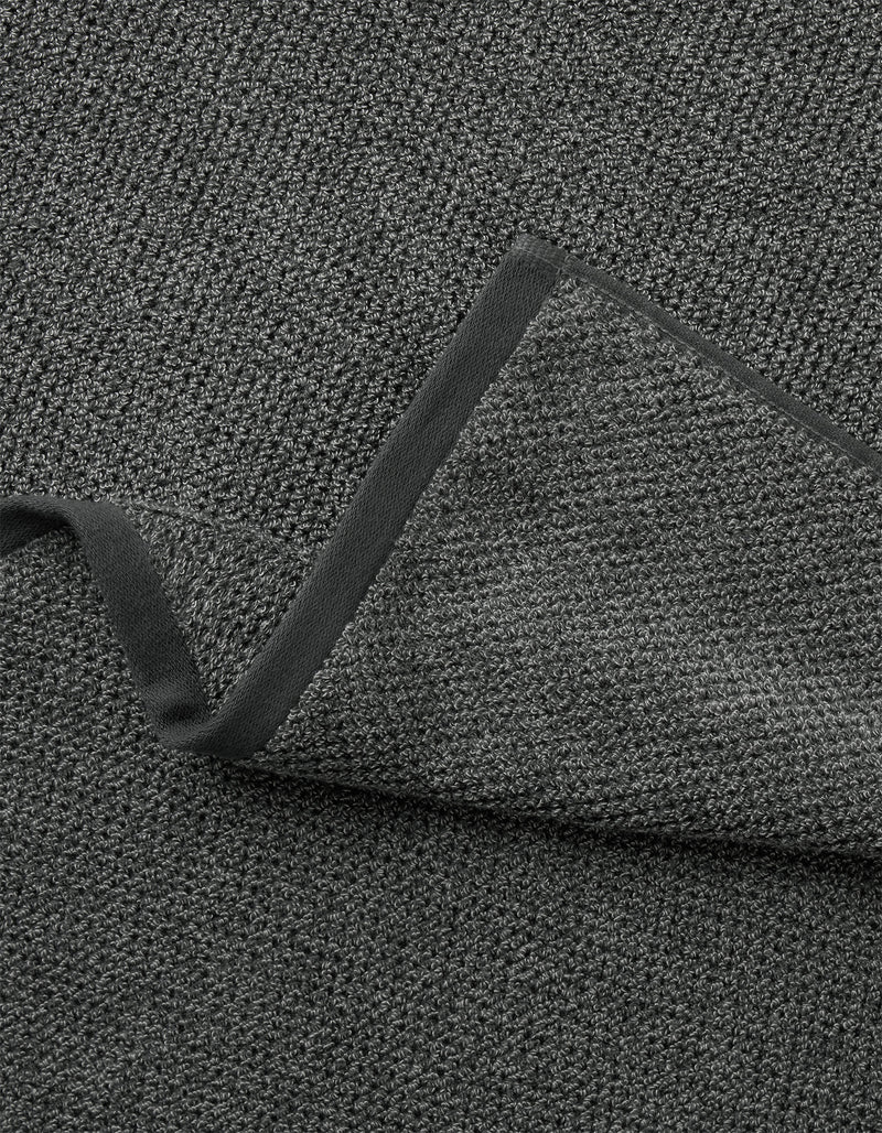 A close-up of the Cozy Earth Nantucket Bath Towel Set in dark gray, showing its textured fabric and black trim, with one corner folded to reveal its thickness.