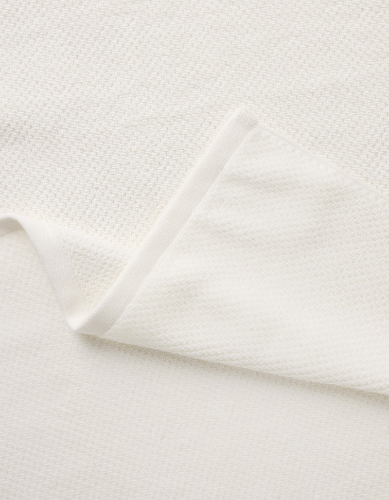 A close-up of the Nantucket Bath Towel Set by Cozy Earth shows its soft, white textured fabric, with a folded corner revealing the towel’s thickness and elegant woven pattern.