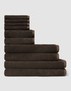 The Cozy Earth Complete Ribbed Terry Bath Bundle, featuring dark brown towels in assorted sizes, is neatly stacked from largest to smallest against a plain light gray background.|Color:Espresso