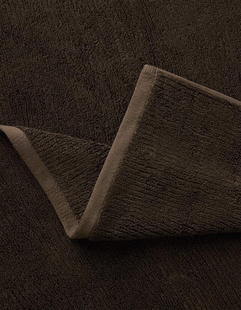 A close-up of the Complete Ribbed Terry Bath Bundle by Cozy Earth in dark brown, featuring one corner folded to reveal its soft ribbed fabric and stitched edges.