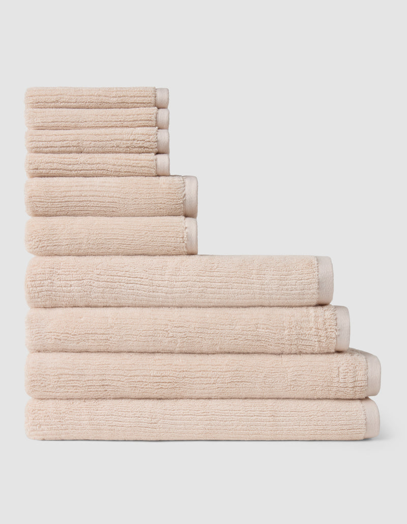 The Complete Ribbed Terry Bath Bundle by Cozy Earth features beige towels in multiple sizes, stacked neatly in a step formation against a plain white background.