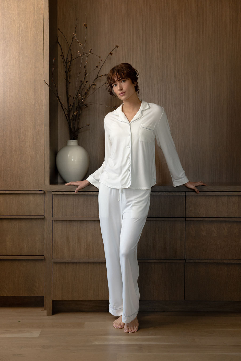 Woman leaning against dresser in ivory pajama set 