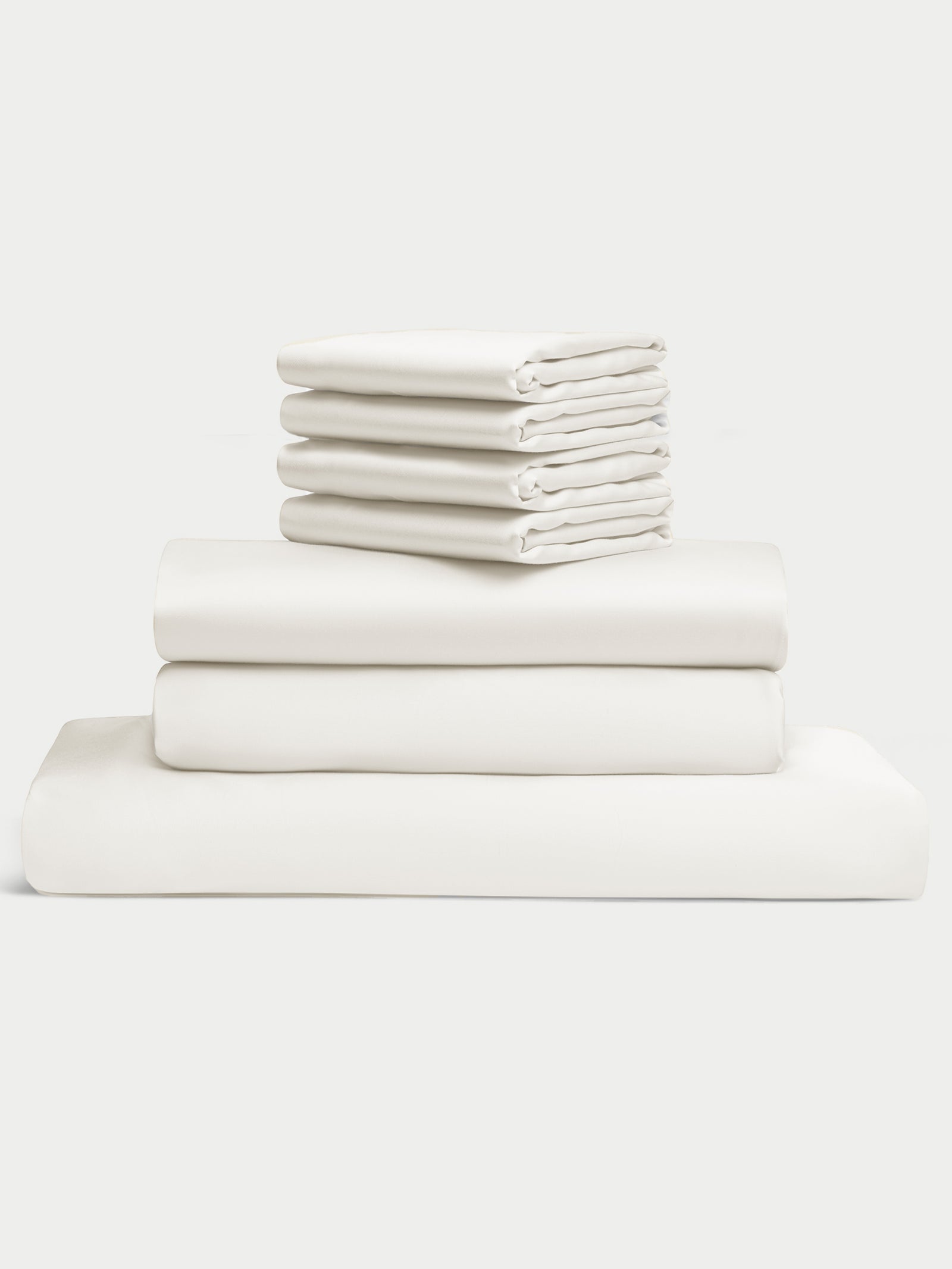 A neatly stacked set of white Bamboo Bedding Core Bundle by Cozy Earth, organized from largest to smallest. The set includes fitted sheets, flat sheets, and pillowcases against a plain light background. 