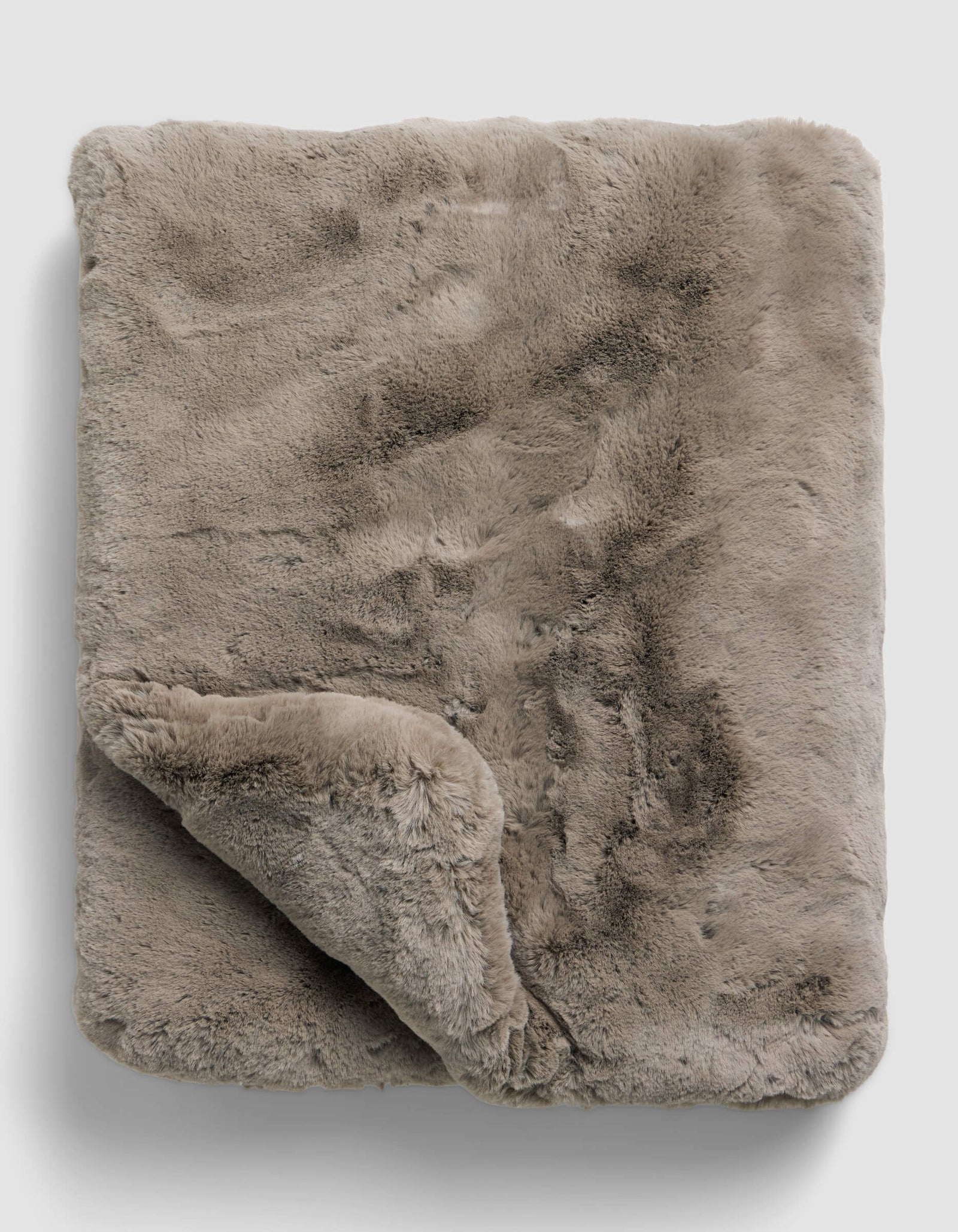 The Superplush Cuddle Blanket by Cozy Earth is a soft, light brown faux fur blanket with a plush texture, shown folded on a plain light gray background. A corner is turned up to reveal its fluffy underside.