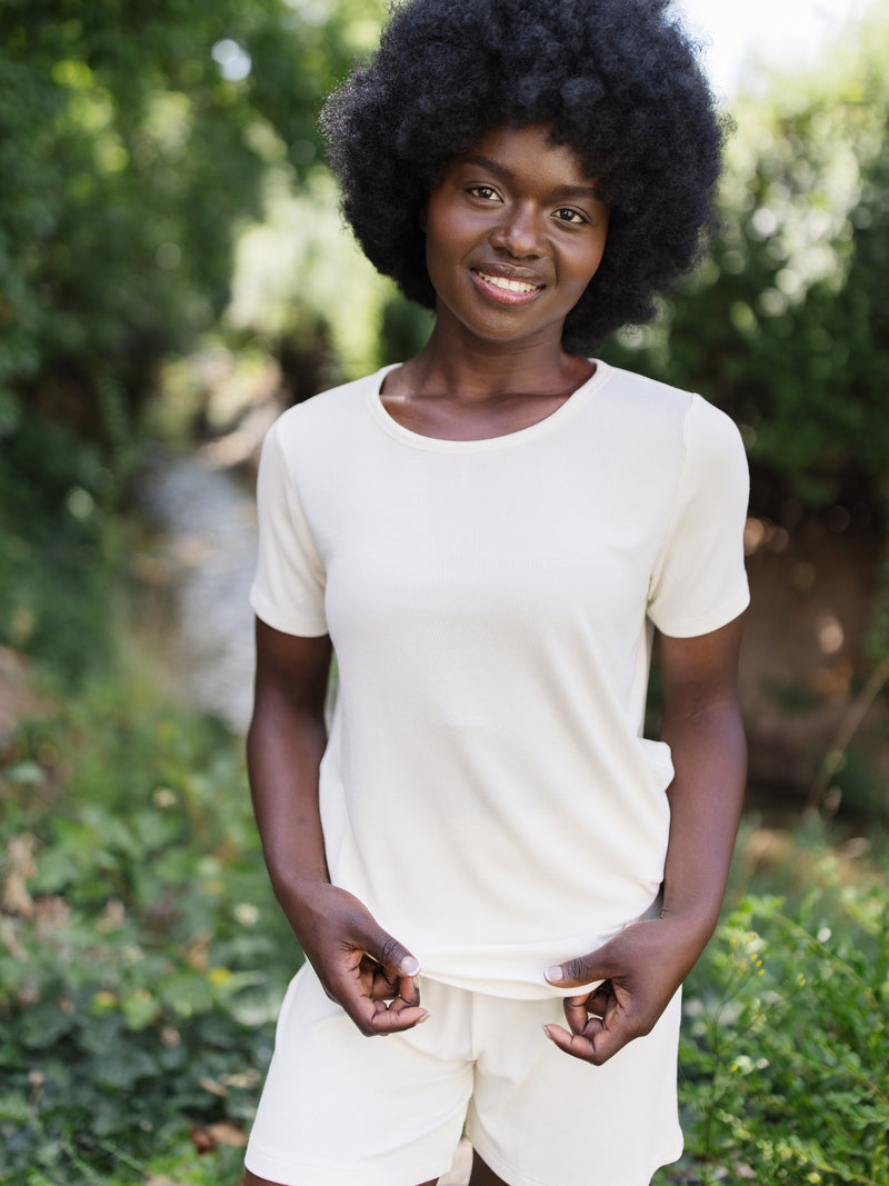 Woman wearing a white Cozy Earth Rib Knit Short Sleeve Lounge Top and white shorts against a garden background