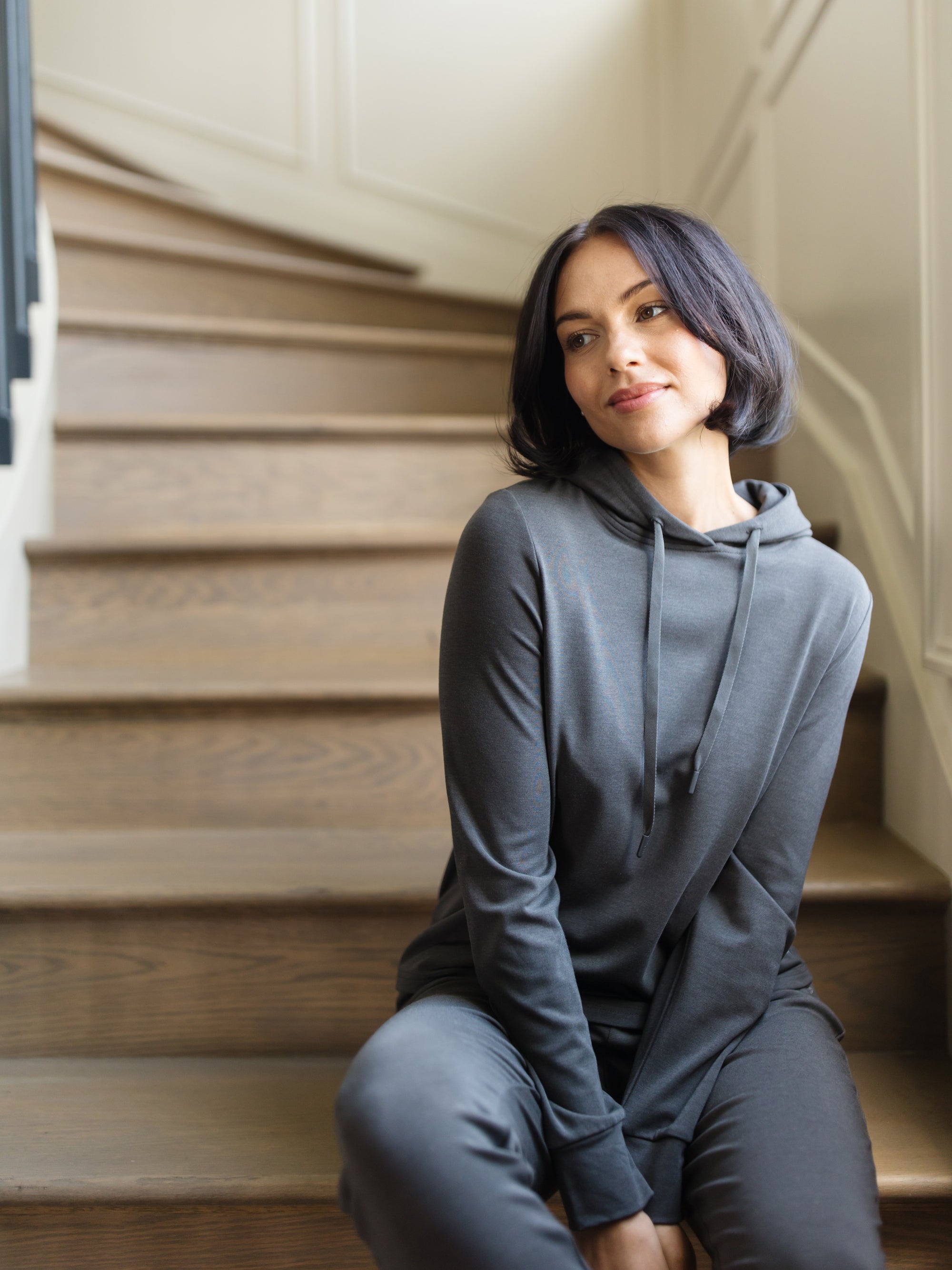 A woman sitting on stairs wearing a grey Cozy Earth Brushed Bamboo Hoodie with a drawstring and sleeve cuffs. 