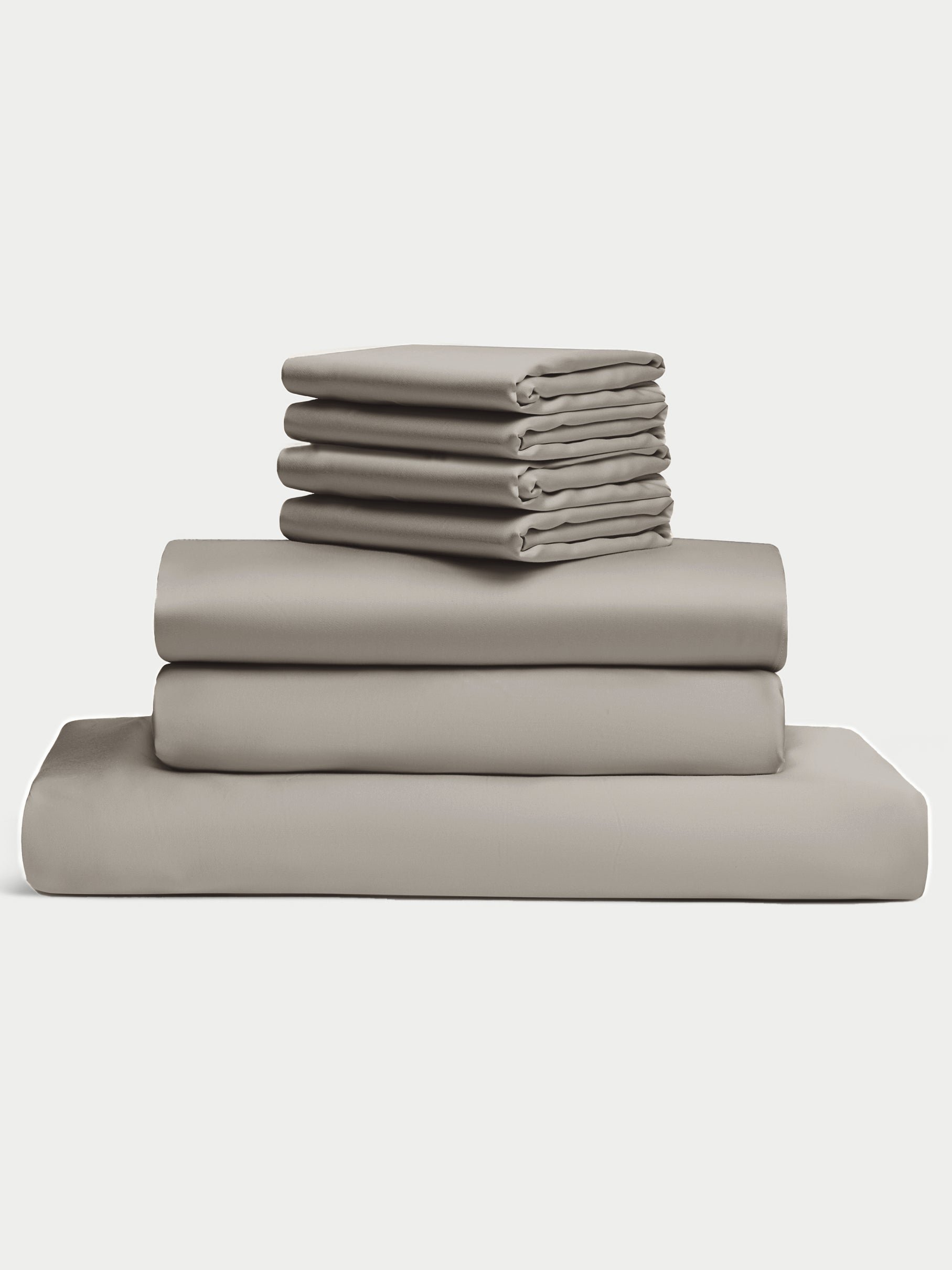A neatly stacked set of five folded bed sheets, featuring Cozy Earth's Bamboo Bedding Core Bundle in gray, lies on a light neutral background. The sheets vary in size, with three larger ones at the bottom and two smaller ones on top. |Color:Dove Grey